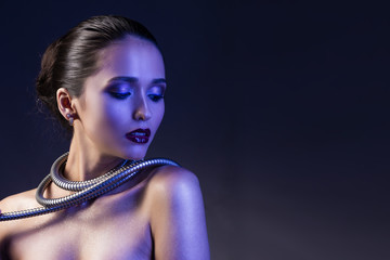 Wall Mural - Beautiful brunette girl with naked shoulders and dark red lips make-up, wears a metal shower spiral hose wrapped around her neck. Concept and advertising low key photo illuminated in blue.