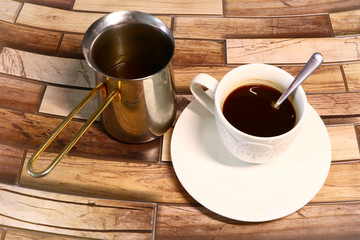 white cup of coffee on a saucer and turkish coffee pot on a wooden background