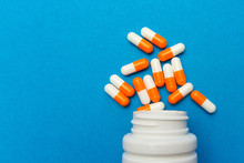 Orange White Capsules (pills) Were Poured From A White Bottle On A Blue Background. Medical Background, Template.