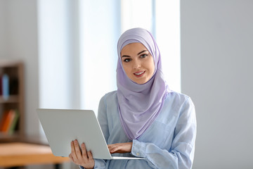 Wall Mural - Muslim student in traditional clothes using laptop indoors