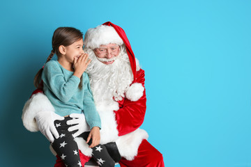 Wall Mural - Little girl whispering in authentic Santa Claus' ear on color background