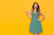 © studioloco - Young Woman In Green Dress Is Looking Away, Pointing And Talking