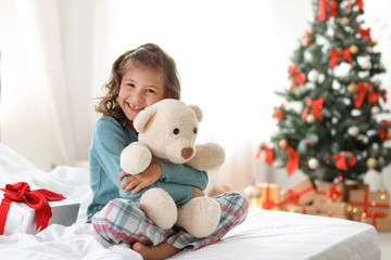 Wall Mural - Cute little child with toy bear and Christmas gift box sitting on bed at home