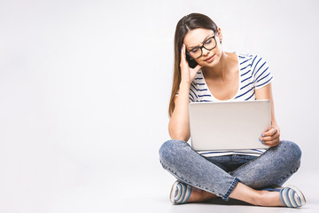 Wall Mural - Business concept. Portrait of depressed woman in casual sitting on floor in lotus pose and holding laptop isolated over white background. Using phone.