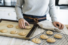Midsection Of Woman Arranging Cookies On Cooling Rack In Kitchen