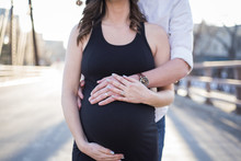 Midsection Of Husband Touching Pregnant Wife's Stomach While Standing On Street