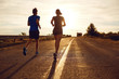 A guy and a girl jog along the road at sunset in nature. The couple is running.