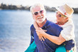 © simona - happy senior couple have fun and enjoy outdoor leisure activity at the beach. the man carry the woman on his back to enjoy together a retired lifestyle at the beach