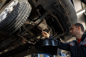 Profecional car mechanic changing motor oil in automobile engine at maintenance repair service station in a car workshop.