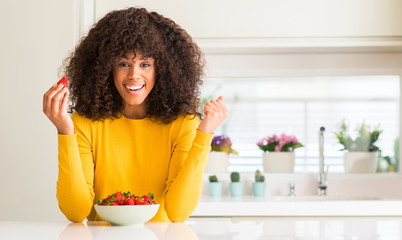 Wall Mural - African american woman eating strawberries at home screaming proud and celebrating victory and success very excited, cheering emotion