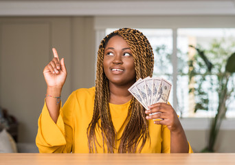 Poster - African american woman holding dollars surprised with an idea or question pointing finger with happy face, number one