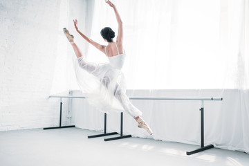 Wall Mural - back view of graceful young ballerina in white dress dancing in ballet studio