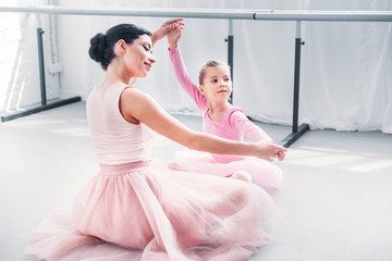 Wall Mural - smiling young ballet teacher and little student in pink tutu skirts training together in ballet school