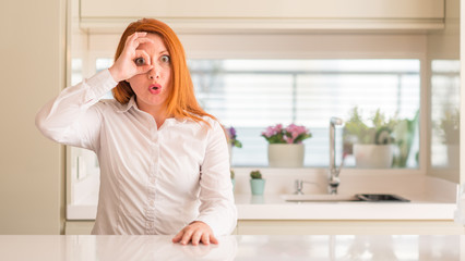 Poster - Redhead woman at kitchen doing ok gesture shocked with surprised face, eye looking through fingers. Unbelieving expression.