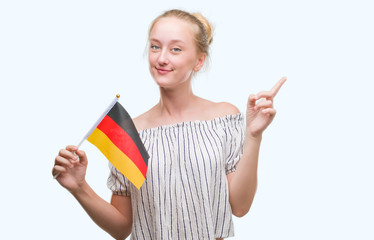 Sticker - Blonde teenager woman holding flag of Germany very happy pointing with hand and finger to the side