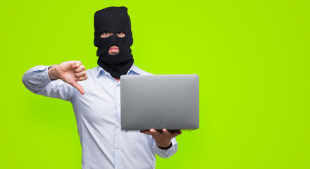 Poster - Business hacker man holding a computer laptop with angry face, negative sign showing dislike with thumbs down, rejection concept