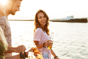 Poster - Happy young friends outdoors on the beach drinking beer.