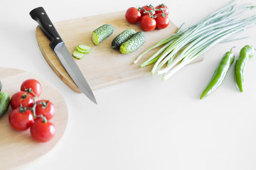 Wall Mural - Vegetables and a knife lie on a wooden board on a white background.