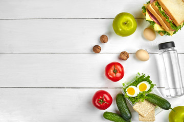 Lunch. Sandwich and fresh vegetables, bottle of water, nuts and fruits on white wooden background. Healthy eating concept. Top view with copy space