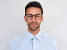 Closeup Headshot Of Handsome Attractive Male, Looks Directly At The Camera, Wears Round Spectacles, Isolated Over White Background. Portrait Of Smart Bristle Student Wearing Casual Blue Shirt. People