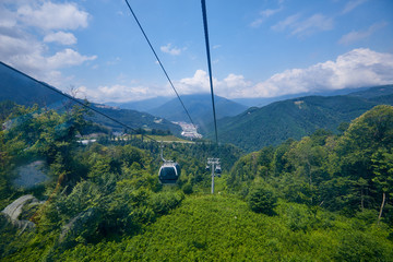 Mountain zipline through autumn forest on backdrop of Caucasus mountains, funicular railway to observation deck tops 2320 m. Krasnaya Polyana - Alpine ski resort. Rosa Khutor, Sochi, Russia