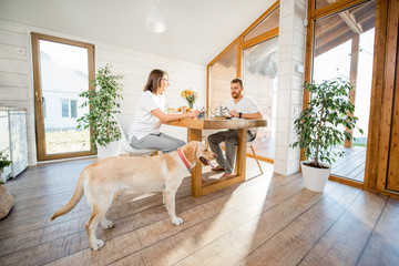 Young couple having a breakfast sitting with dog in the dining room in the wooden country house