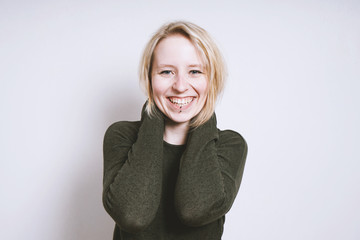 portrait of a blue-eyed blonde happy young woman with big toothy smile from Germany standing in front of interior wall with copy space