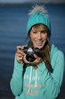 © karrastock - Smiling young woman using a camera to take photo.