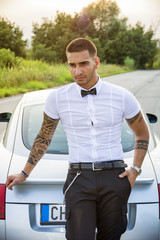 Wall Mural - Portrait of young attractiave man in white shirt leaning on his new stylish polished car outdoor