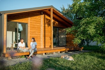 Young lovely couple sitting with dog on the terrace on the backyard of their wooden country house