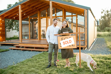 Elegant and happy couple standing in front of their new and beautiful wooden country house