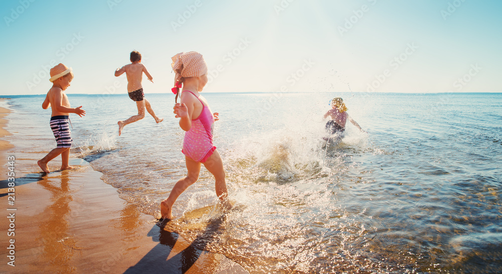 Happy kids on vacations at seaside running in the water - obrazy, fototapety, plakaty 