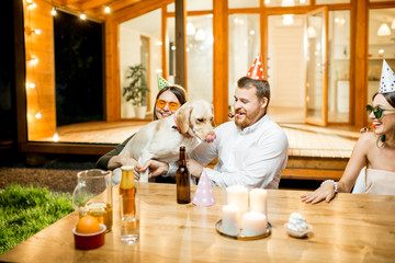 Wall Mural - Funny dog with young couple sitting at the table during a celebration on the backyard of the house outdoors