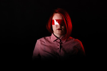 Red hair girl in dark studio with red color clothes, close portrait, woman in t-shirt and jeans. Face with Scotch tape on eyes. Censored theme