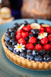 Delicious, mouthwatering and colorful Summer Berry Tart, topped with Blueberry and Raspberry, decorate with cute flower on a turquoise blue plate. Selective focus.