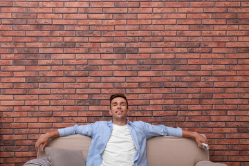 Wall Mural - Young man relaxing under air conditioner on brick wall at home