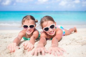 Close up little girls on sandy beach. Happy kids lying on warm white sandy beach