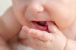 Small cute funny baby infant teething with face expression hands and fingers in mouth sore gums