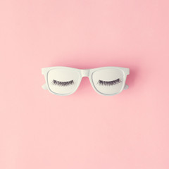 Wall Mural - Creative layout made of white painted sunglasses and eyelashes on pastel pink background. Minimal flat lay.