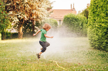 Child Playing With Garden Sprinkler, Jumping Over