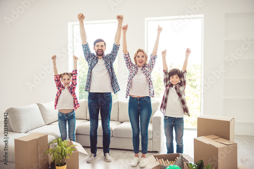 Success concept. Young happy smiling caucasian family wearing casual moving to new flat, standing toghether raising hands up in light living room