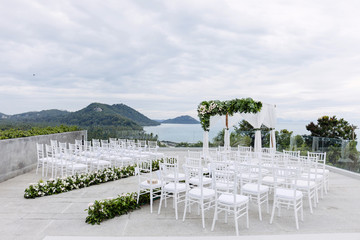 Wall Mural - Wedding venue setting on the hill, white chairs with flowers decoration, ocean background