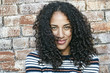 © Mint Images - Portrait of young smiling woman with long curly black hair, looking at camera.