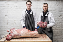 Two Young Men Working, Butchers Jointing A Whole Lamb Carcass. 