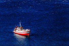 Aerial View Of Red Fishing Boat On A Deep Blue Sea In Greece.
