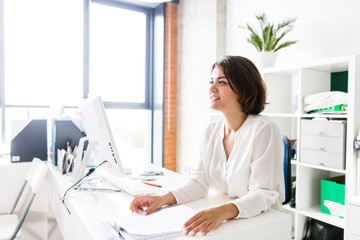 Wall Mural - Business lady in a white blouse sitting at a table in the office