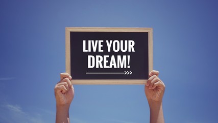 Wall Mural - Motivational and inspirational quote - ‘LIVE YOUR DREAM’ written on a blackboard. Background of blue sky.