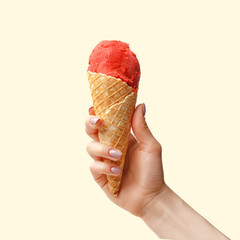 Wall Mural - Female hand with a horn of strawberry ice cream on a light pink background