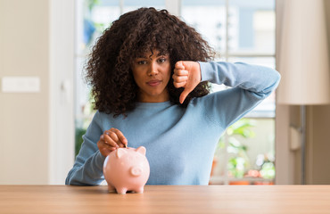 Poster - African american woman saves money in piggy bank with angry face, negative sign showing dislike with thumbs down, rejection concept