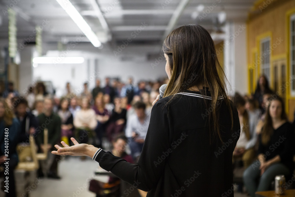 Woman gives a public speech in front of 200 people, in an industrial environment - obrazy, fototapety, plakaty 